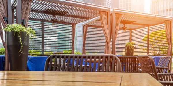 Outdoor seating area with wooden tables and pergolas in soft sunlight.