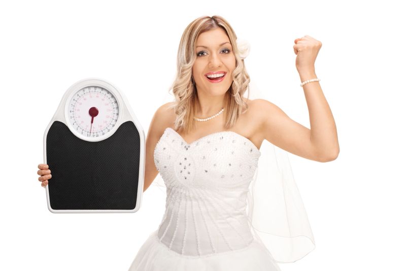 Joyful bride holding a weight scale and gesturing happiness isolated on white background