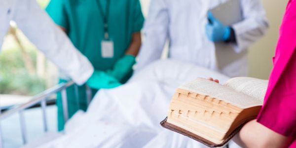 Medical professionals gathered around a patient, one holding an open book.