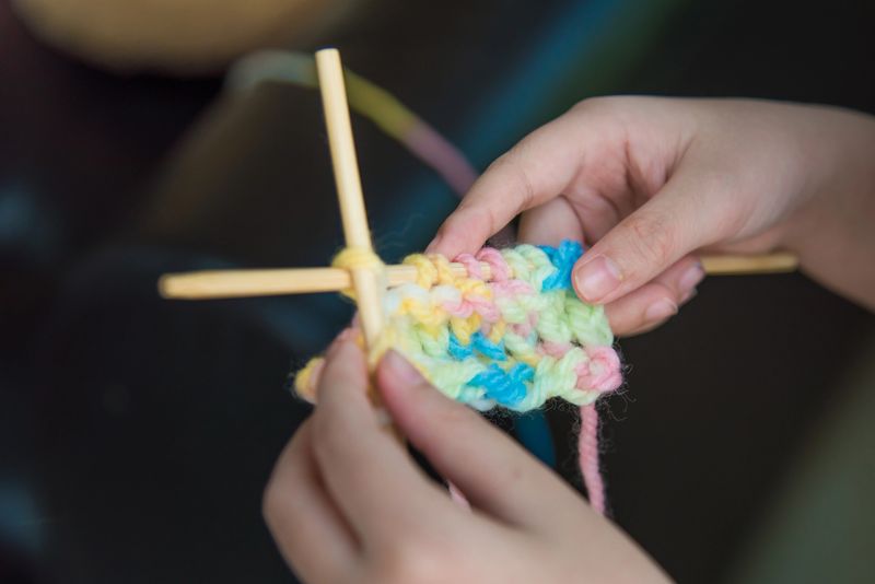 Close up of children hand try to knitting the colorful yarn.