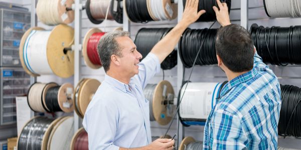 Two men selecting cables from large spools in a store.