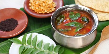 Traditional South Indian Rasam served with curry leaves and spices on a banana leaf.