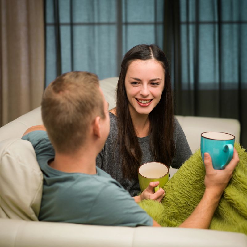 young happy couple on couch drinking tea at home and laughing