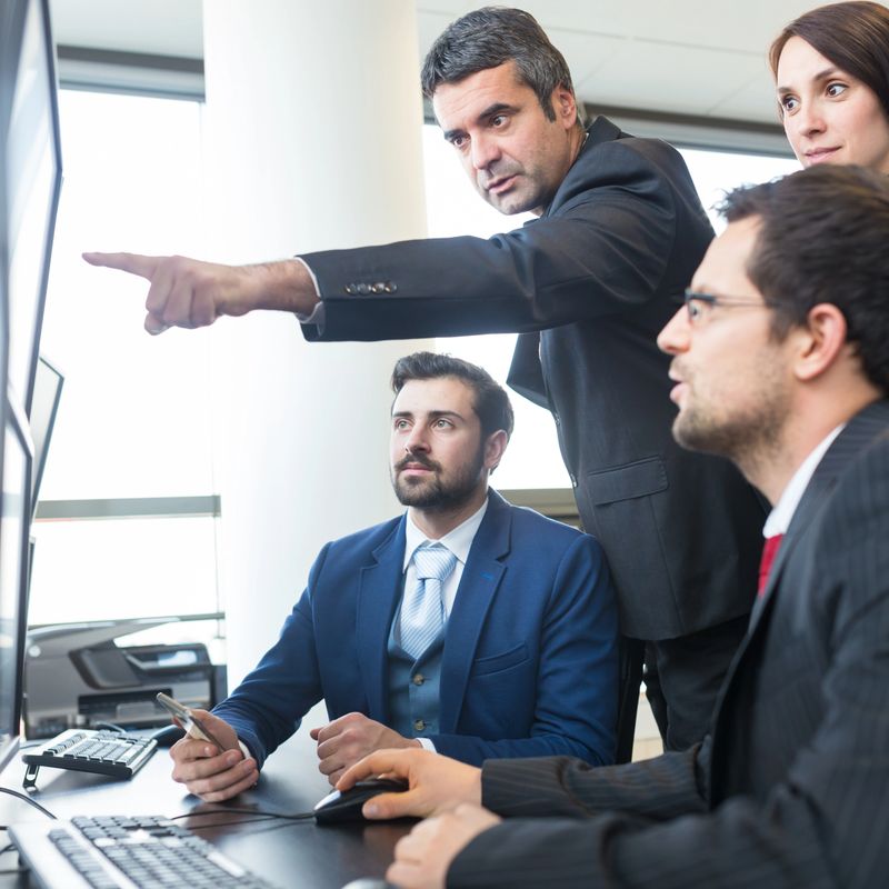 Business team looking at data on multiple computer screens in corporate office. Businessman pointing on screen. Business people trading online. Business, entrepreneurship and team work concept.