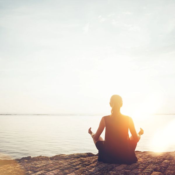 Person meditating by the water at sunrise.