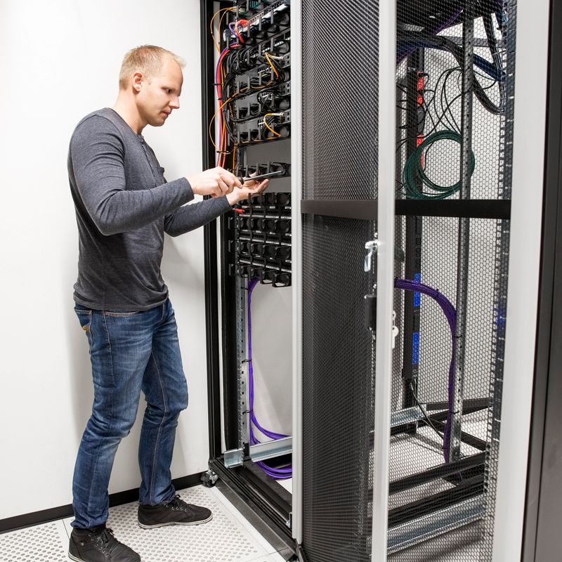 IT engineer or technician working with network cabling and installation communication switches in datacenter.