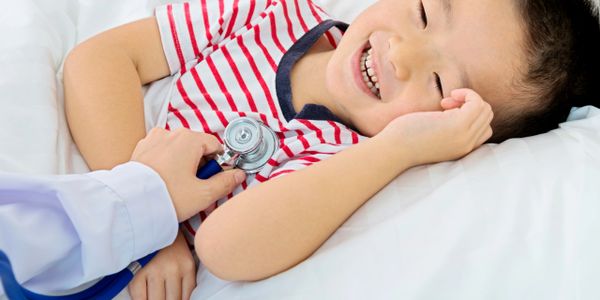 Child smiling while doctor checks heartbeat with stethoscope.