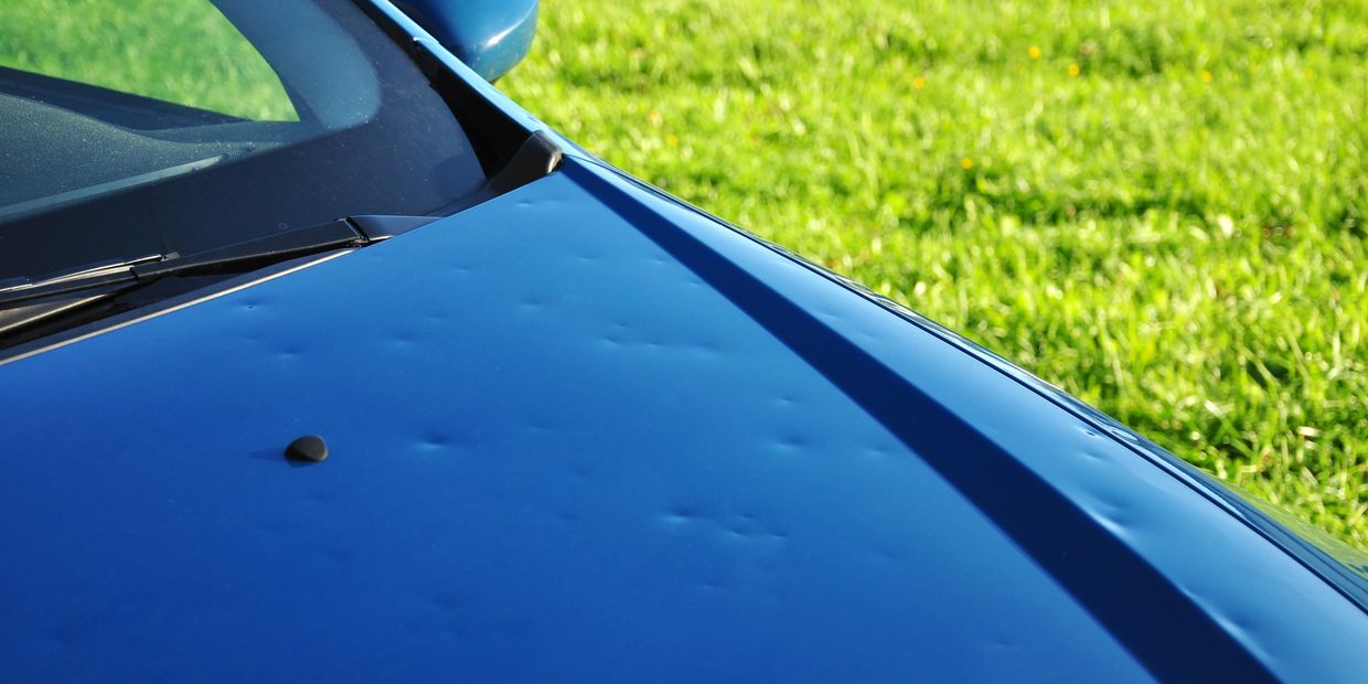 Close-up of a blue car hood with multiple small dents.