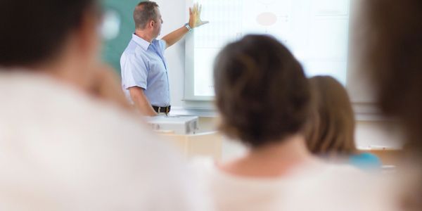 Male instructor presenting information to an audience in a classroom setting.