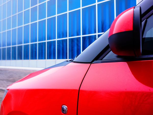 Close-up of a red car parked near a modern blue glass building.