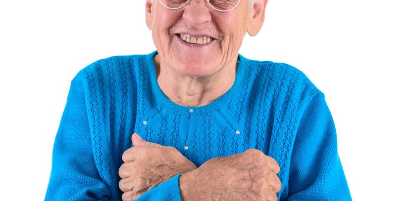 Elderly woman in blue sweater smiling warmly with arms crossed over her chest.
