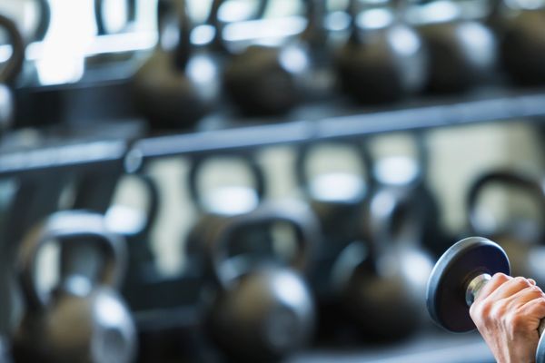 Woman lifting a dumbbell in a gym with kettlebells in the background.