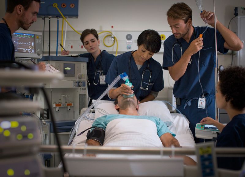 Doctor holding mask over patients mouth and doctor controlling IV drip in intensive care unit