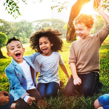 Three happy children playing and laughing together outdoors on a sunny day.