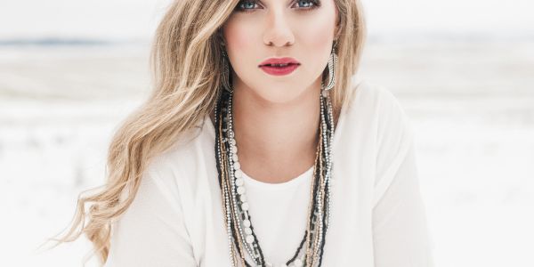 Portrait of a woman with long blonde hair and layered necklaces in a snowy background.