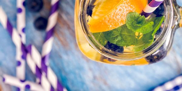 Refreshing citrus and blueberry drink with mint in a glass jar and purple-striped straws.