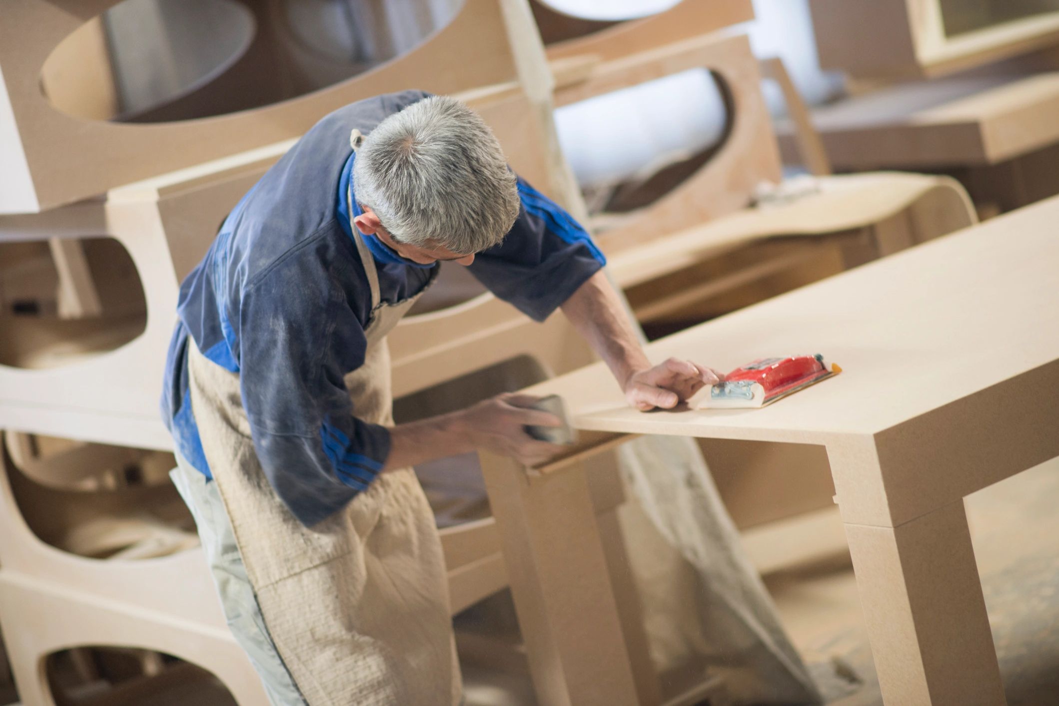 Carpintero lijando una mesa de madera clara.
