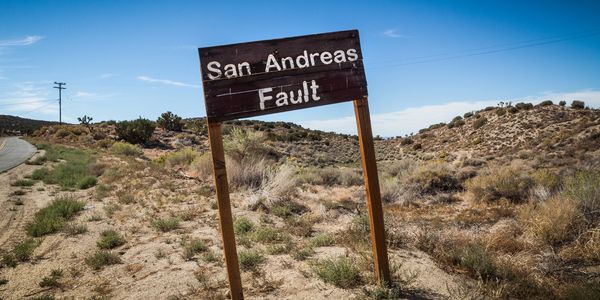 Worn San Andreas Fault sign in arid desert landscape under clear blue sky.