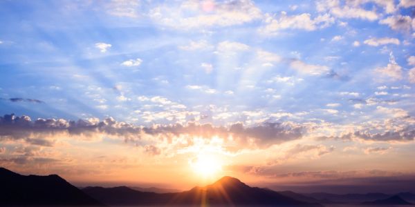 Sunrise over mountain peaks with scattered clouds in the sky.