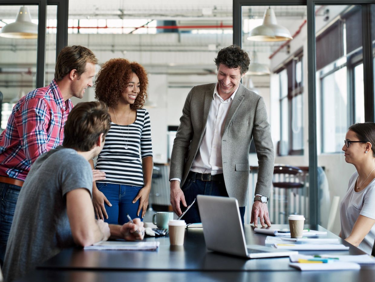A group of five diverse colleagues enjoying a lively meeting in a modern office.