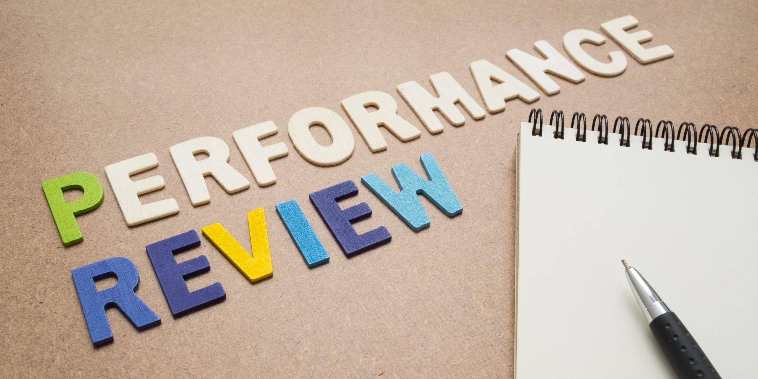 Wooden letters spelling 'Performance Review' next to a pen and notepad.
