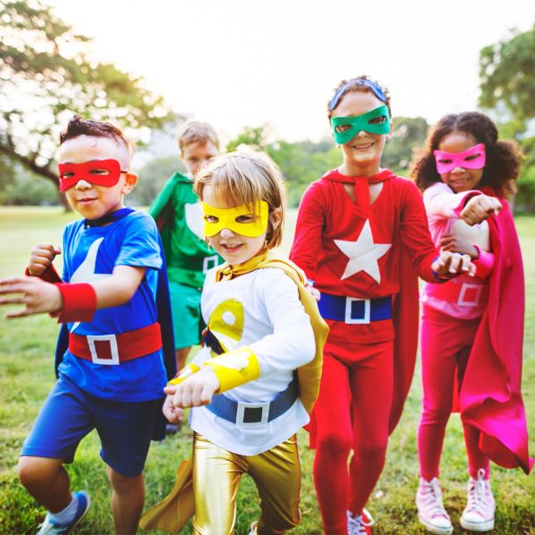 Kids dressed as colorful superheroes playing outdoors.