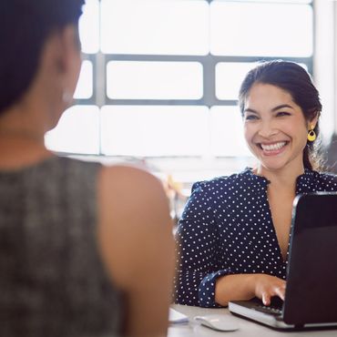 Smiling woman in polka dot shirt using laptop during a conversation.