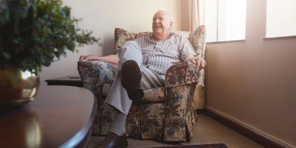 Elderly man sitting comfortably in a floral armchair by the window.
