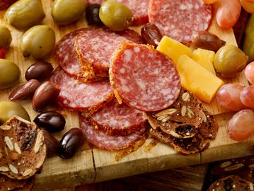 A charcuterie board with sliced salami, olives, cheese, grapes, and crackers.
