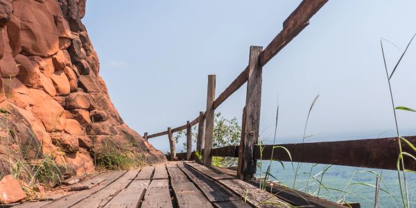 Wooden pathway with railing along rocky cliff and ocean view.