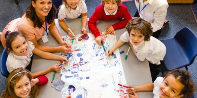Smiling children and teachers collaborating on a colorful drawing in a classroom.
