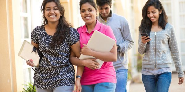Group of young people walking outdoors while carrying laptops and phone.