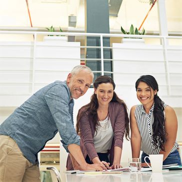 Three colleagues smiling and collaborating at a meeting table in a modern office.
