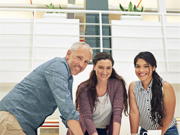 Three colleagues smiling and collaborating at a meeting table in a modern office.