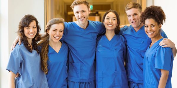 Smiling healthcare workers in blue scrubs standing together in a hospital corridor.