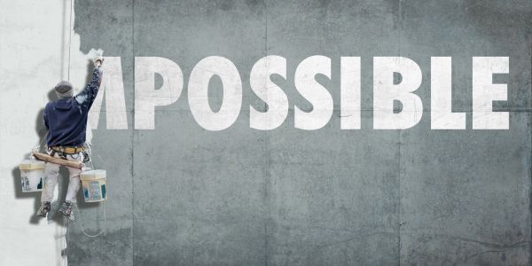 Man painting over part of the word "IMPOSSIBLE" on a wall.