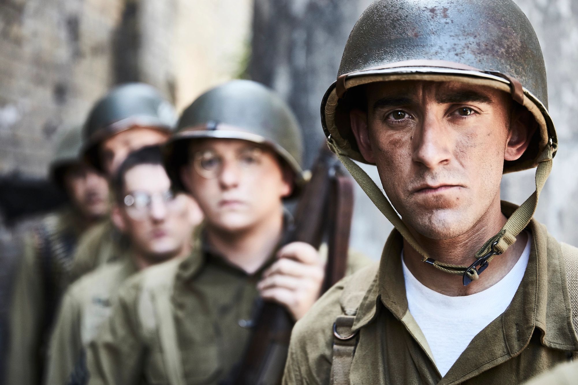 Soldiers in vintage military helmets lined up, one in sharp focus.