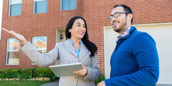 Real estate agent showing a house to a potential buyer outside a brick home.