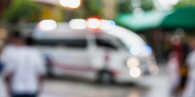 Blurred image of a police vehicle with flashing lights and people nearby outdoors.