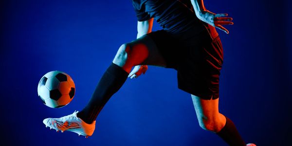 Soccer player in black outfit controlling the ball mid-air with dramatic lighting.