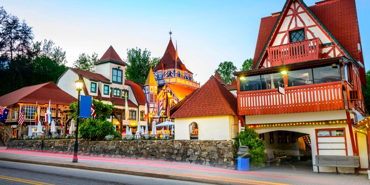 Colorful, fairy-tale style buildings along a street with flags and outdoor seating.