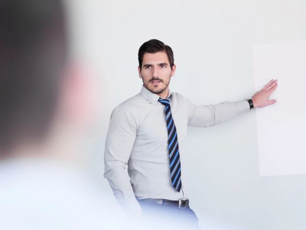 A man in a dress shirt and tie giving a presentation with a whiteboard.