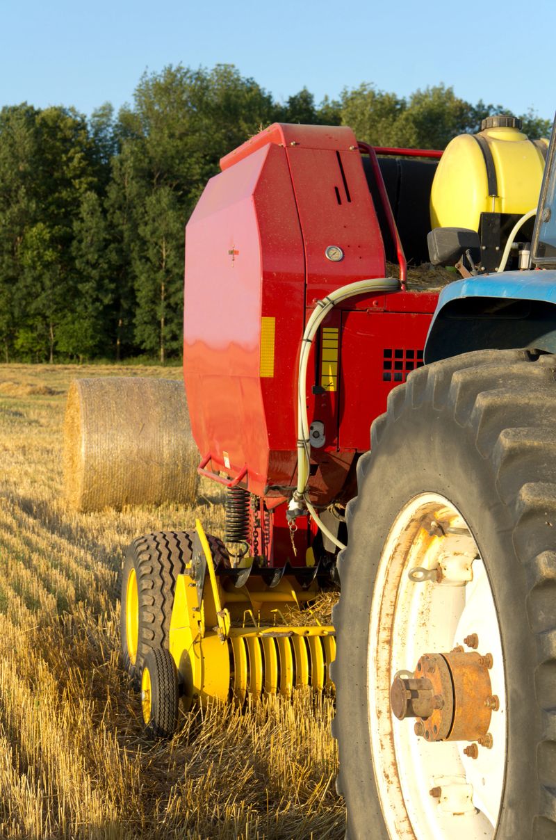 Close up view of a farm tractor pulling a round baling machine in a wheat field after harvest. 