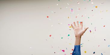 A hand raised in celebration with colorful confetti falling around it.