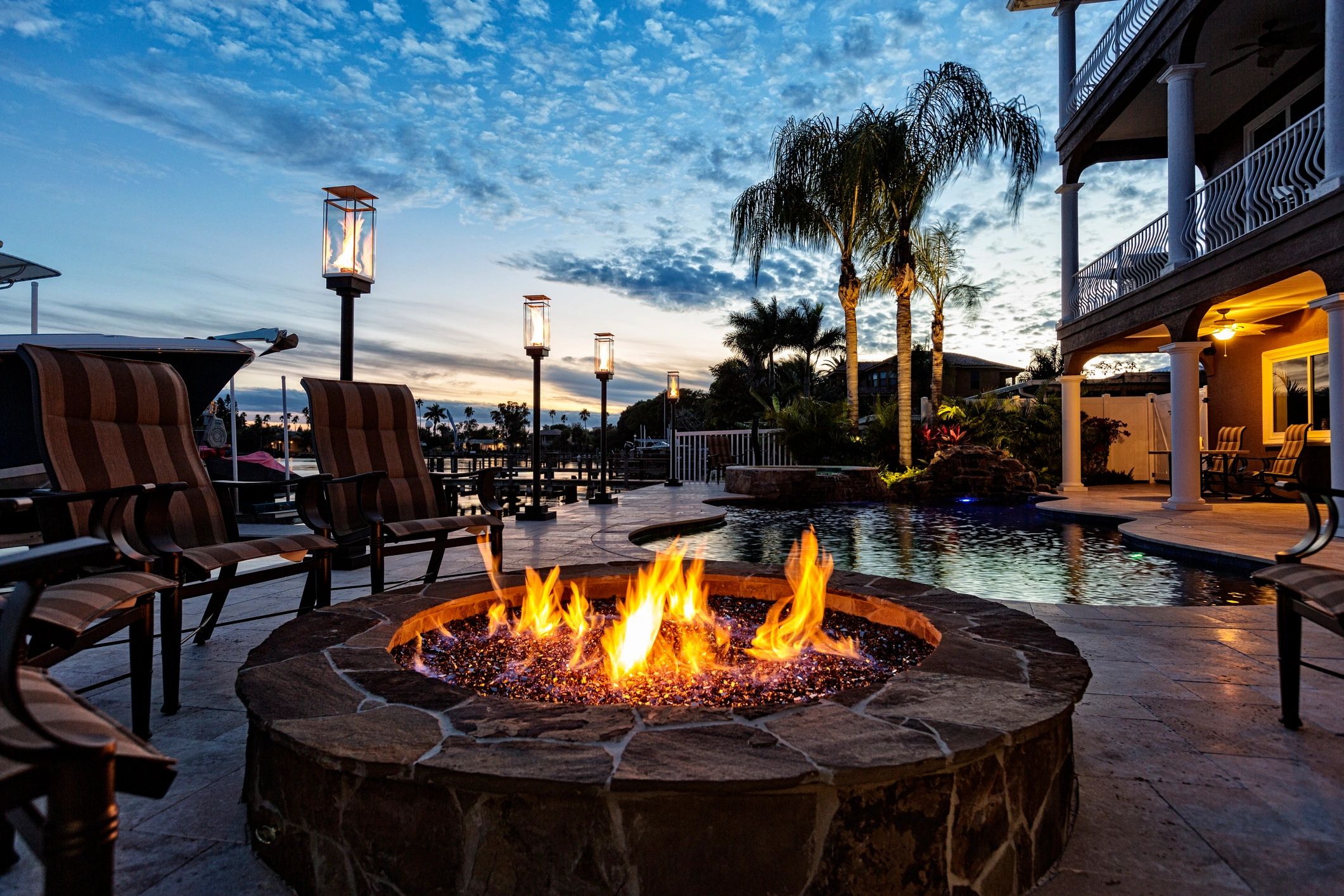 Cozy fire pit by poolside at sunset with palm trees and lanterns.