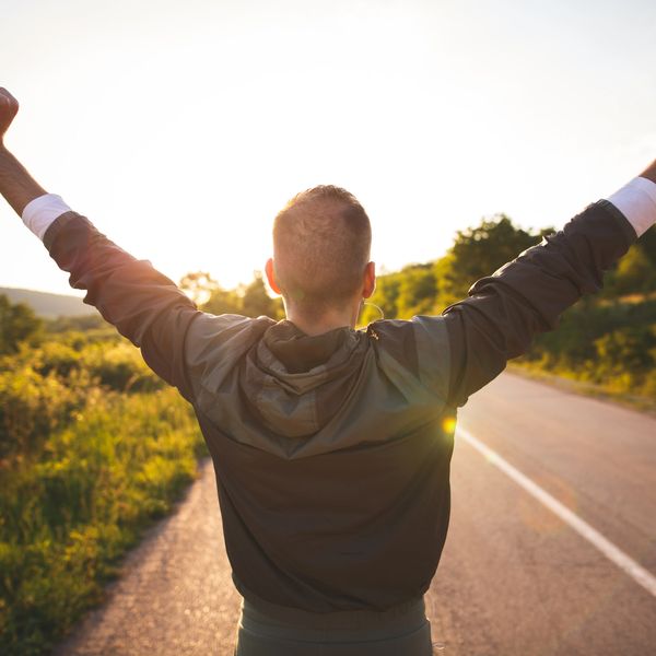 A man stands victorious on the side of a road after completing a workout.