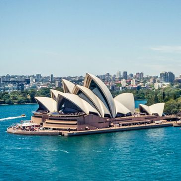 The Sydney Opera House with its white sail-like roofs set against a bright blue sky and harbor.