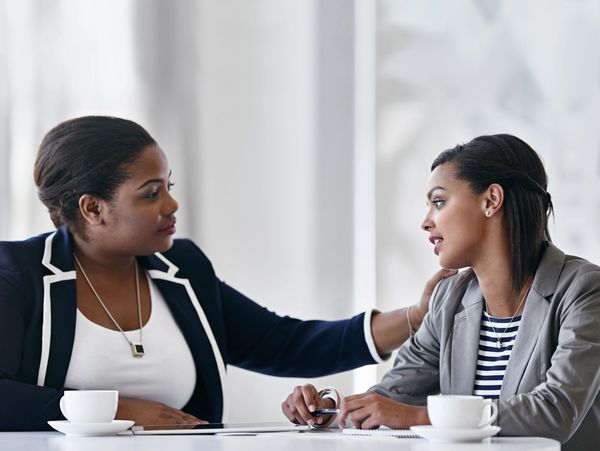 Two professional women share a supportive moment during a meeting.