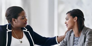 Two women engaged in a supportive conversation in a bright office.
