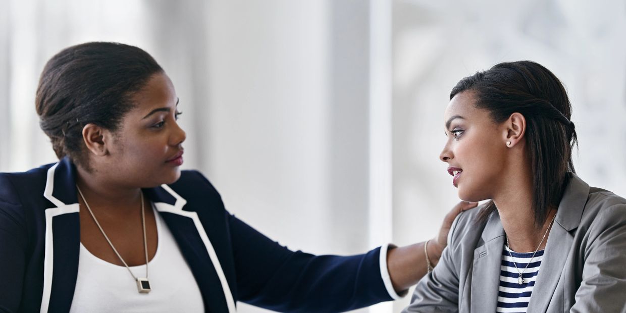 Two women engage in a supportive conversation, one comforting the other with a hand on her shoulder.